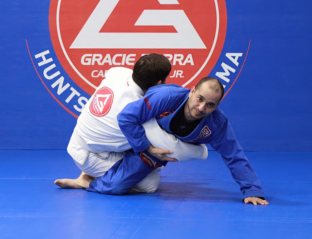 Two adults training Brazilian Jiu-Jitsu in front of the Gracie Barra Huntsville mat logo